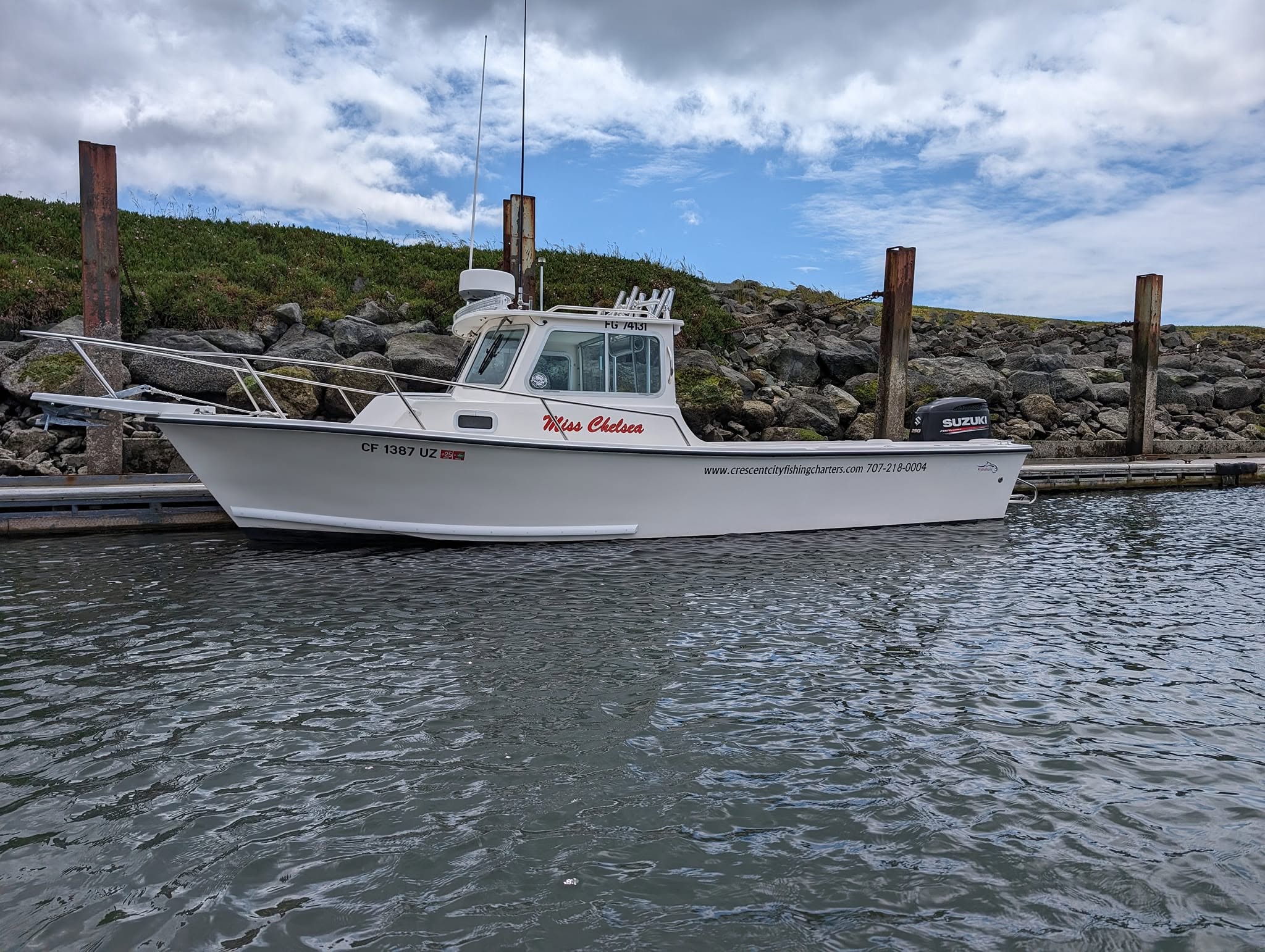 Charter fishing boat "Miss Chelsea" docked near rocky shoreline, showcasing its equipment and service information for potential customers.