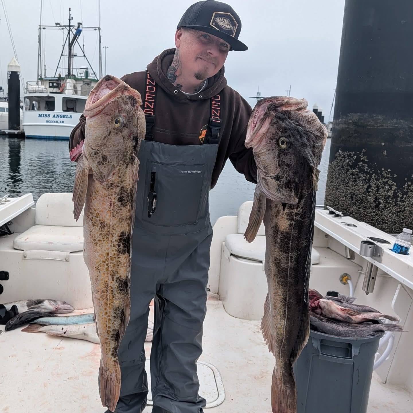 Man on a fishing boat proudly holds two large cod fish, showcasing his catch against a misty harbor backdrop. Ideal for fishing enthusiasts.
