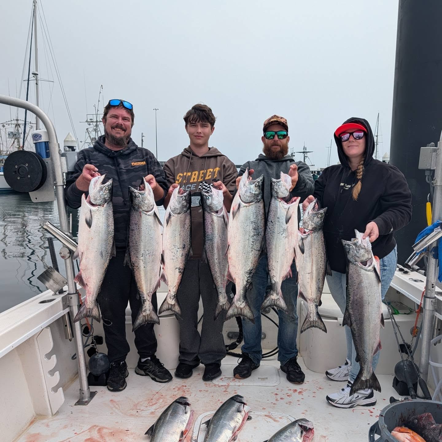 Four individuals proudly display a large catch of salmon onboard a fishing boat, showcasing their successful outing.