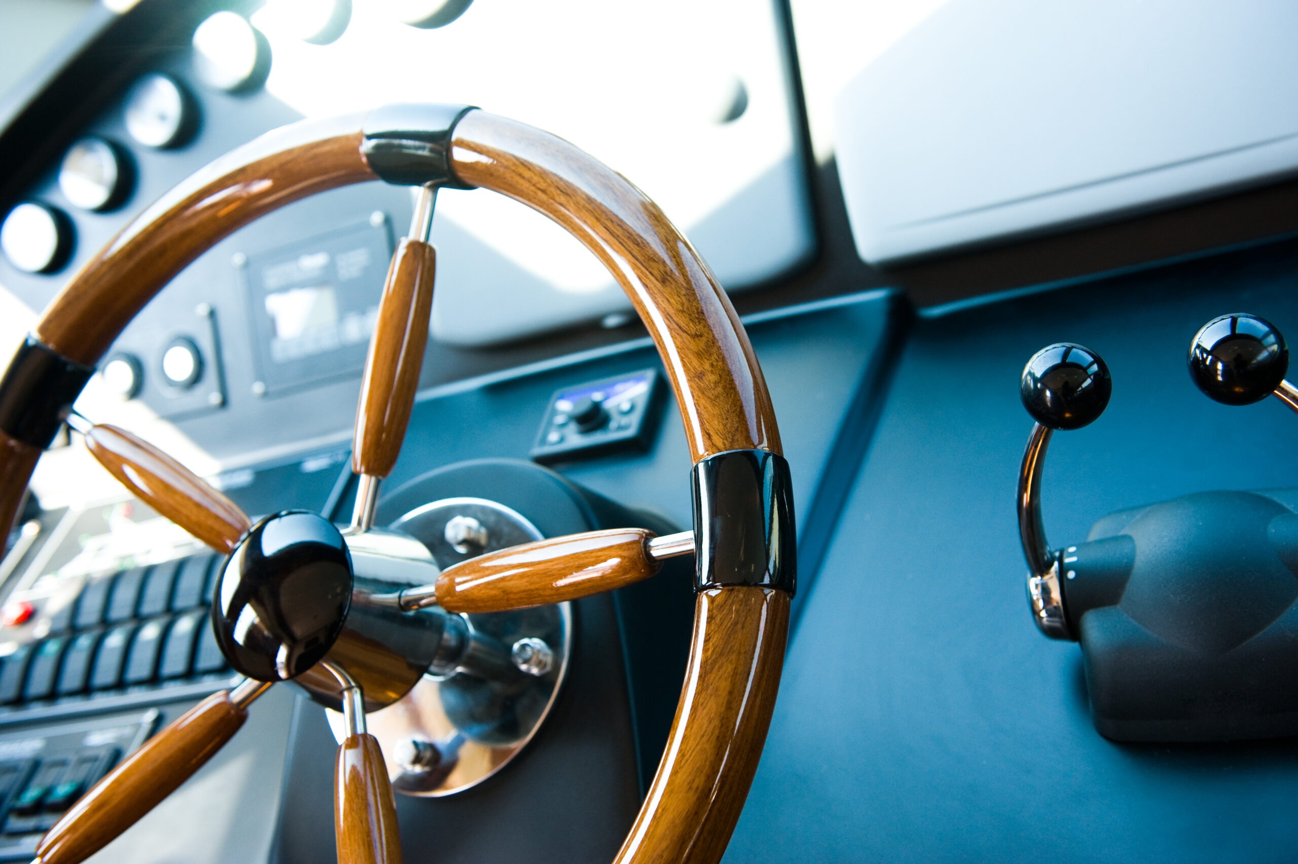 Close-up of a wooden steering wheel and control panel, showcasing the cockpit of a boat, emphasizing high-end design and functionality.